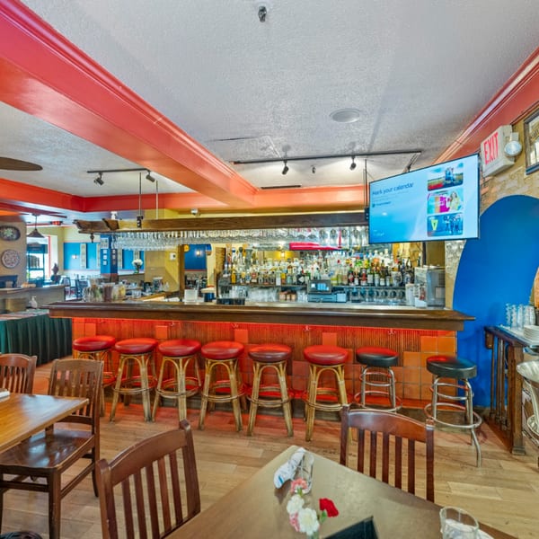 Interior of Guapo's Cocina & Bar, featuring a long, fully stocked bar with red stools and wooden tables.