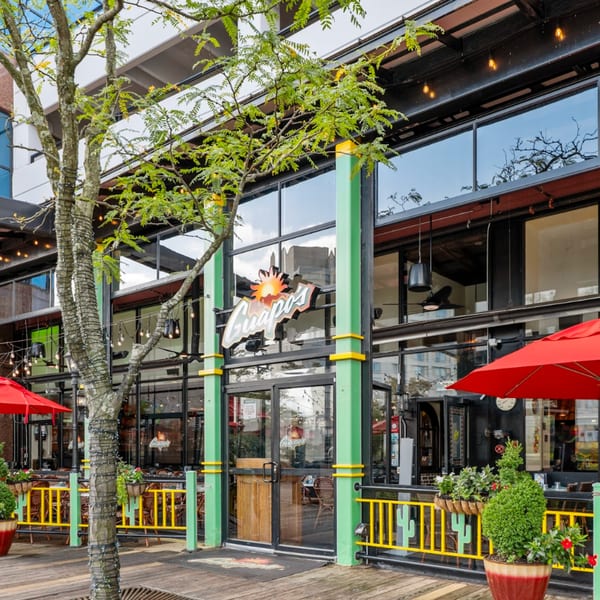 Exterior of Guapo's Cocina & Bar with a large glass facade, outdoor patio, and red umbrellas.