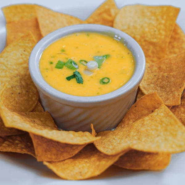 Guapo's Cocina & Bar's queso dip with green onions, surrounded by crispy tortilla chips.