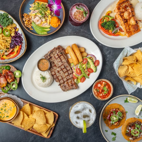 Overhead view of a spread of Mexican dishes including steak, tacos, ceviche, and drinks.