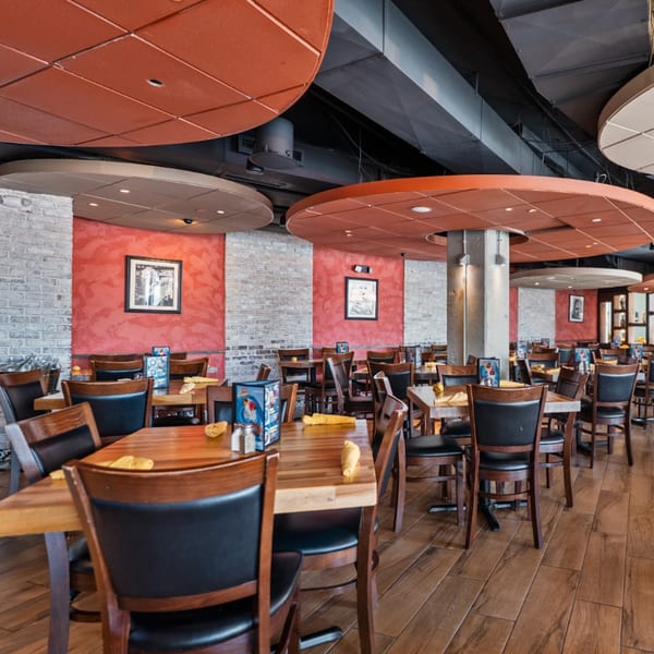 Guapo's Cocina & Bar dining room with wooden tables, black chairs, brick walls, and red accents.